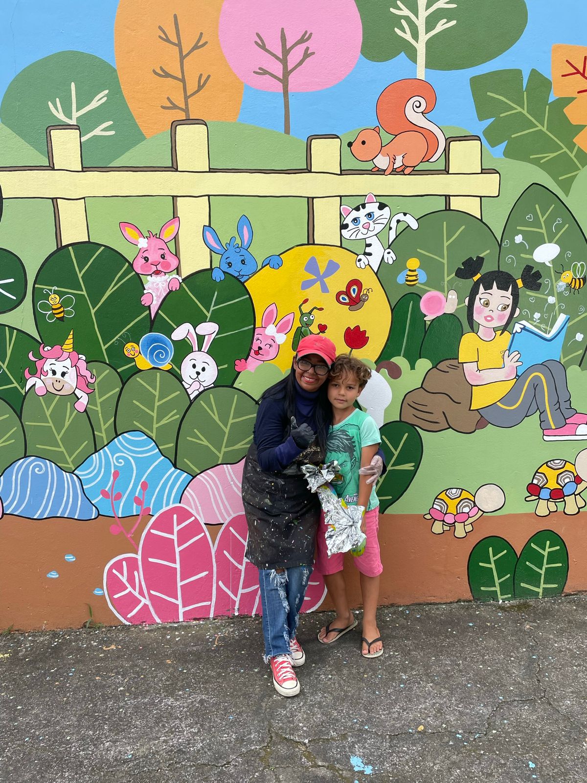 Voluntária e criança com ovo de Páscoa em frente a mural pintado