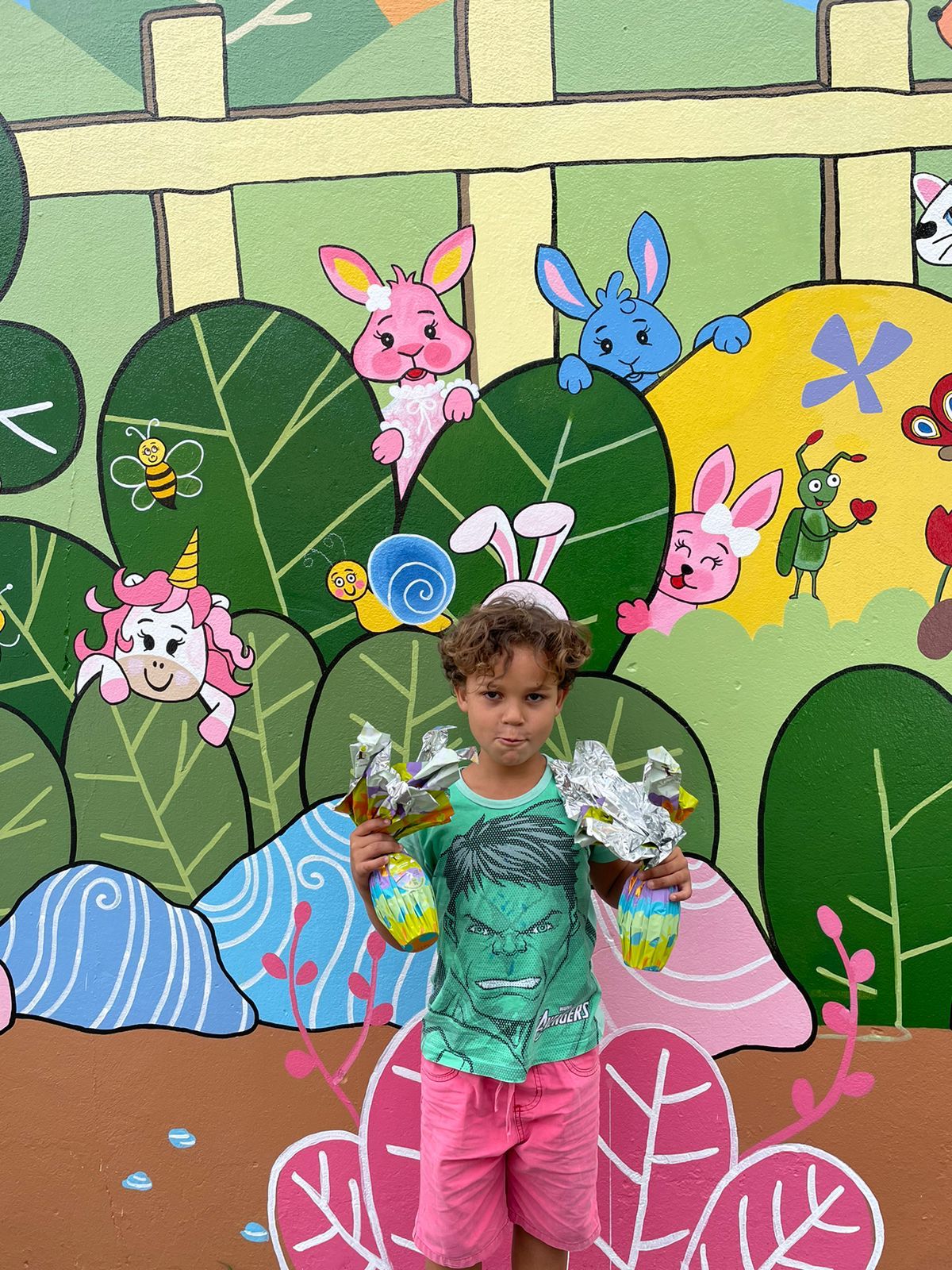 Menino com ovos de Páscoa Cacau Show diante de mural colorido